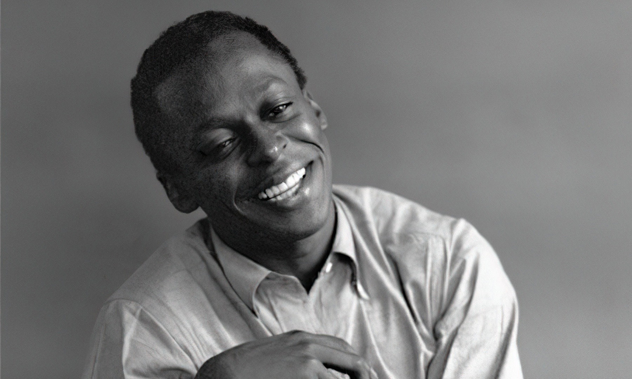 Black and white portrait of Miles Davis smiling, tilting his head.