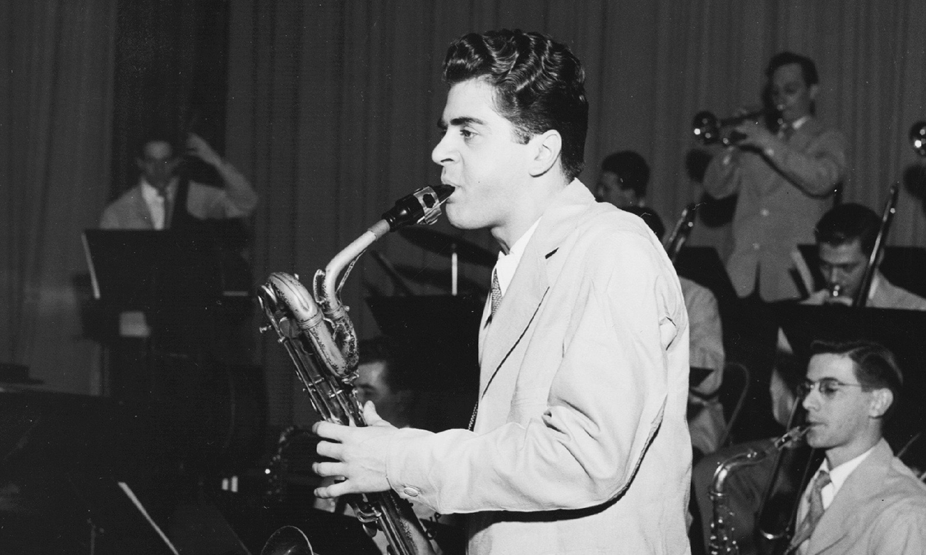 Black and white photograph of Charlie Mariano playaing the saxophone in a brass ensemble.