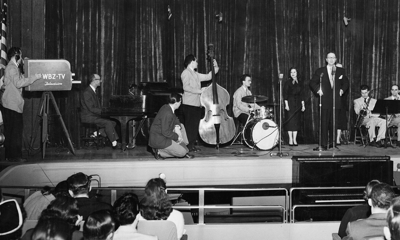 Black and white photograph of musicians performing on stage from the perspective of the audience.