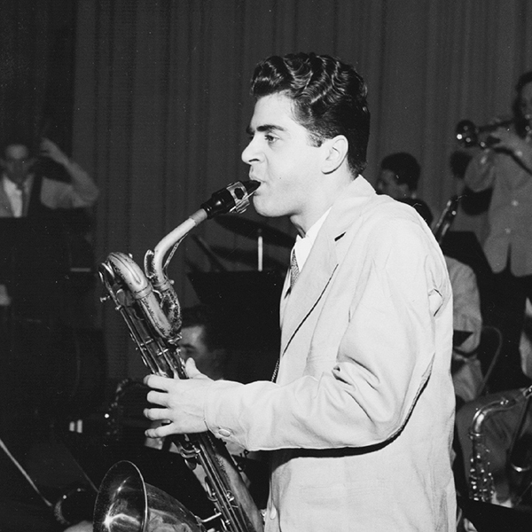 Black and white photograph of Charlie Mariano playaing the saxophone in a brass ensemble.