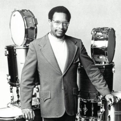 Black and white portrait of Alan Dawson standing in front of drums.